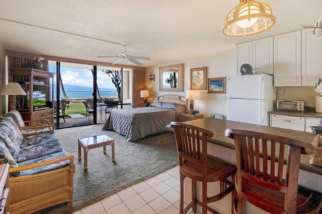 bedroom with freestanding refrigerator, access to outside, a water view, light tile patterned floors, and a textured ceiling