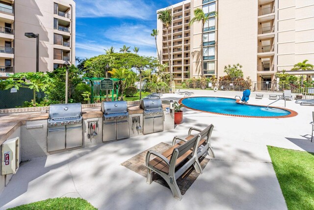 community pool with grilling area, an outdoor kitchen, fence, and a patio