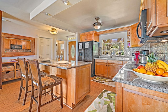 kitchen with tasteful backsplash, stone countertops, light wood-style floors, a breakfast bar area, and black appliances