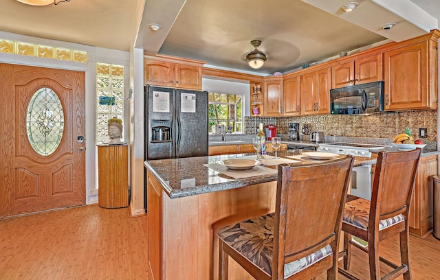 kitchen with black appliances, backsplash, a sink, and light wood-style floors