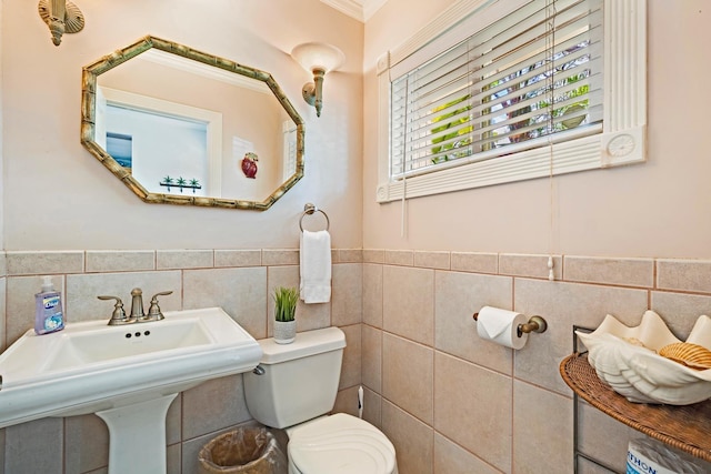 half bathroom featuring toilet, a wainscoted wall, a sink, and tile walls