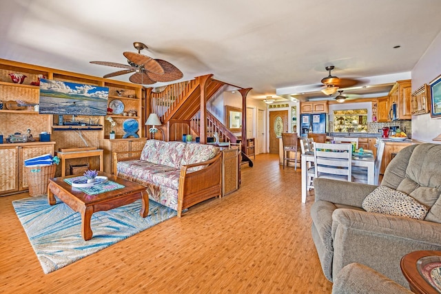 living room featuring a ceiling fan, light wood-style floors, and stairway