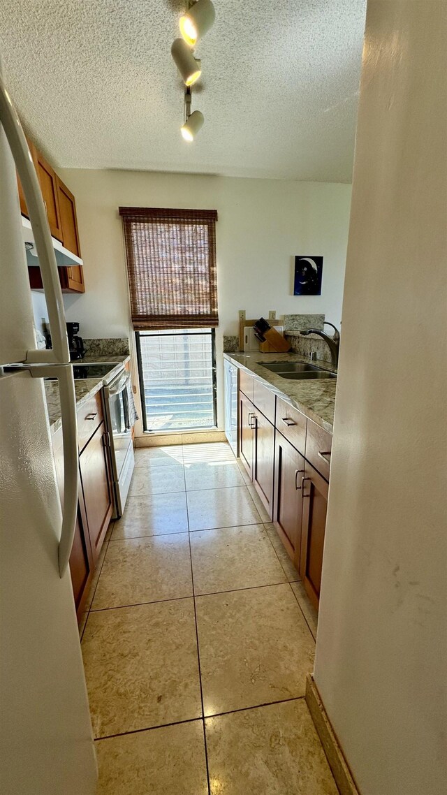 kitchen with sink, light tile patterned floors, stainless steel electric range oven, a textured ceiling, and white fridge