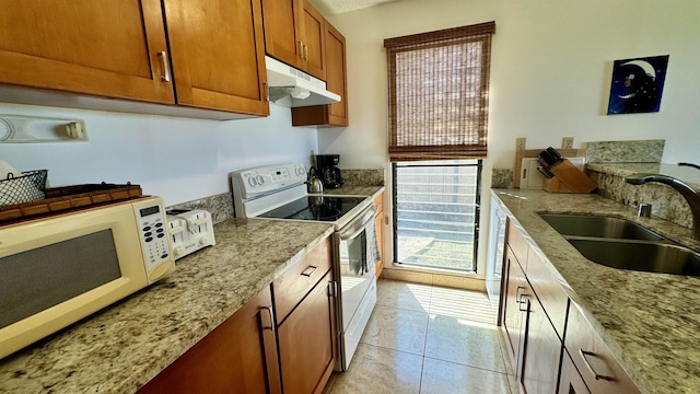 kitchen with white appliances, light tile patterned floors, light stone countertops, under cabinet range hood, and a sink