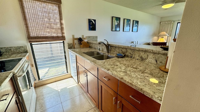 kitchen with light tile patterned floors, light stone countertops, a sink, brown cabinets, and white electric range oven