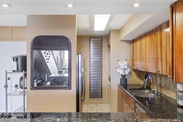 kitchen with backsplash, dark stone countertops, brown cabinetry, a textured ceiling, and a sink