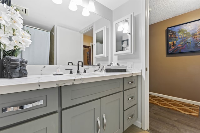 full bathroom with a textured ceiling, vanity, baseboards, and wood finished floors