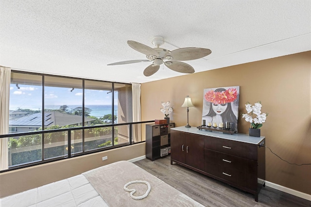 bedroom featuring ceiling fan, wood finished floors, baseboards, and a textured ceiling