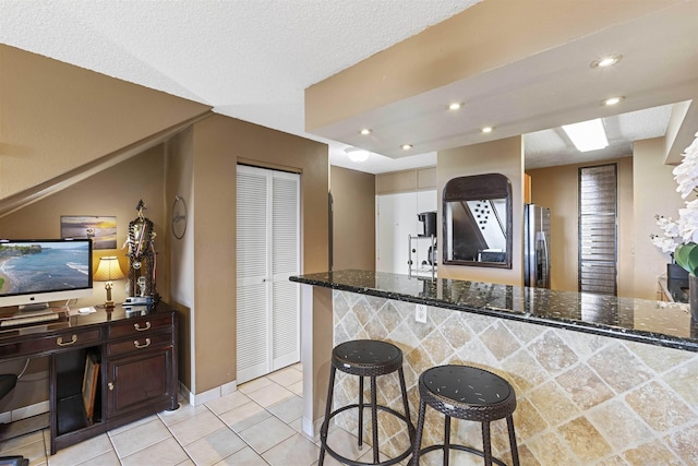 kitchen with a kitchen bar, dark stone counters, light tile patterned flooring, and freestanding refrigerator