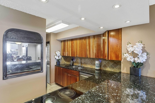 kitchen featuring a sink, dark stone countertops, tasteful backsplash, stainless steel dishwasher, and brown cabinetry