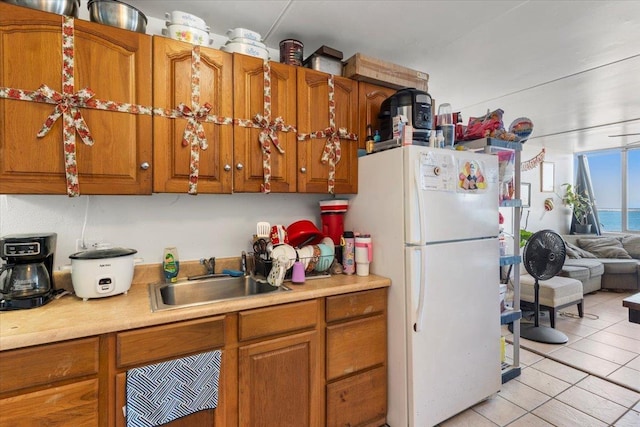 kitchen with white refrigerator, a water view, light tile patterned floors, and sink