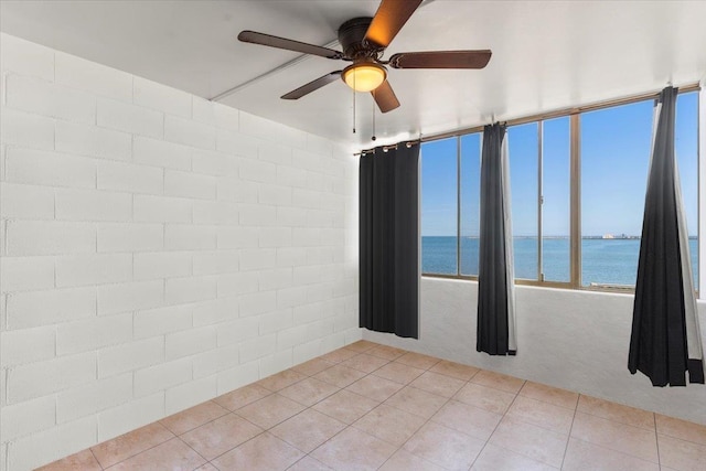 tiled empty room featuring a water view and ceiling fan