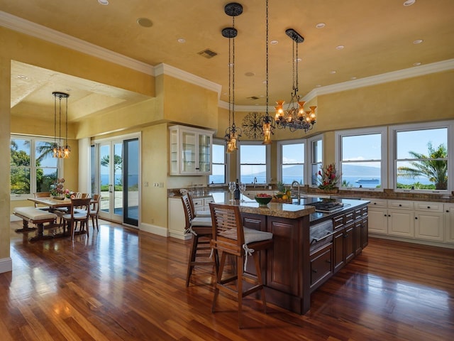 kitchen featuring white cabinetry, a kitchen island, a kitchen breakfast bar, dark stone counters, and a water view