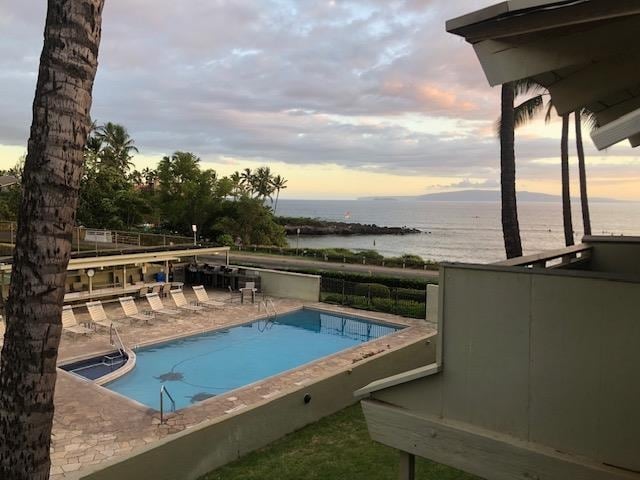 pool at dusk featuring a water view and a patio area