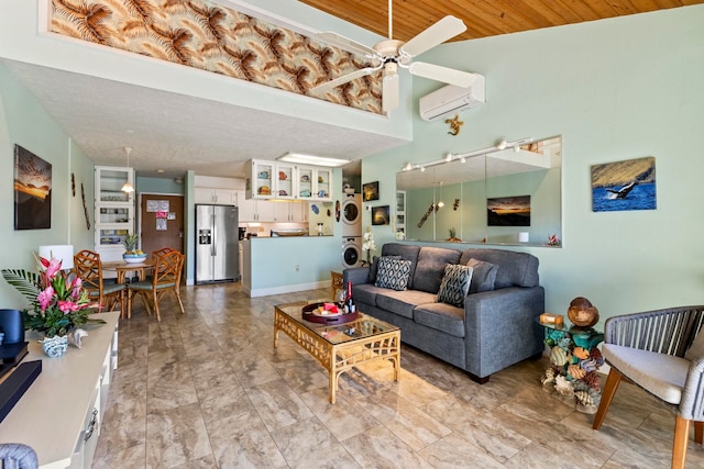 living room featuring wood ceiling, ceiling fan, stacked washer / dryer, and a wall mounted AC