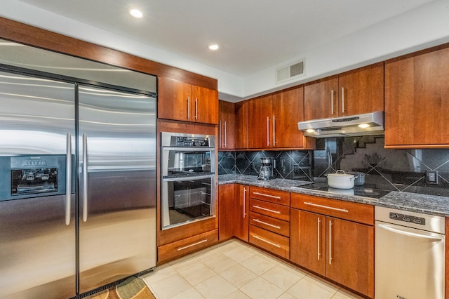 kitchen with tasteful backsplash, dark stone countertops, light tile patterned floors, and stainless steel appliances