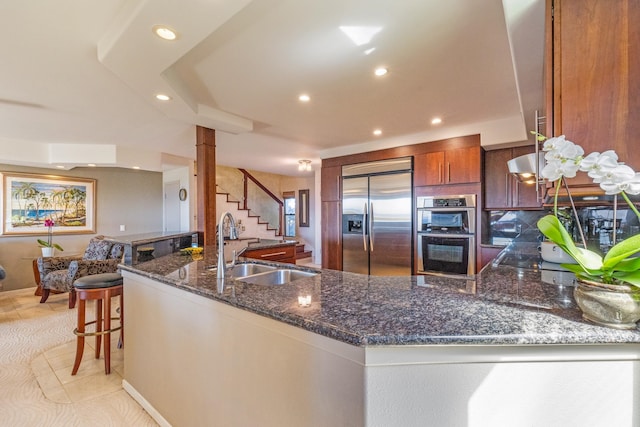 kitchen with kitchen peninsula, a kitchen breakfast bar, stainless steel appliances, sink, and dark stone countertops