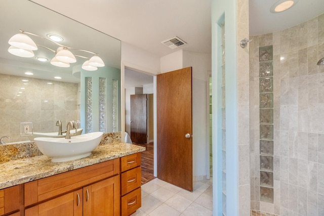 bathroom with tile patterned floors, vanity, tiled shower, and tile walls