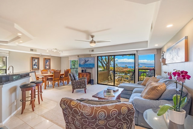 tiled living room with a tray ceiling and ceiling fan