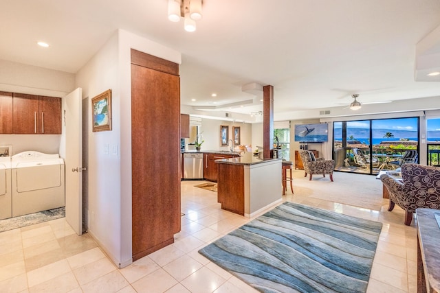 kitchen featuring washer and clothes dryer, stainless steel dishwasher, ceiling fan, light tile patterned flooring, and kitchen peninsula