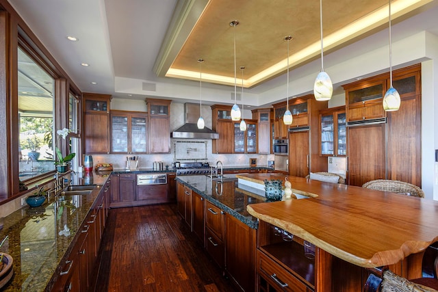 kitchen featuring an island with sink, pendant lighting, a tray ceiling, and wall chimney exhaust hood