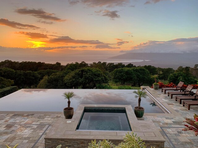 pool at dusk featuring an in ground hot tub and a patio