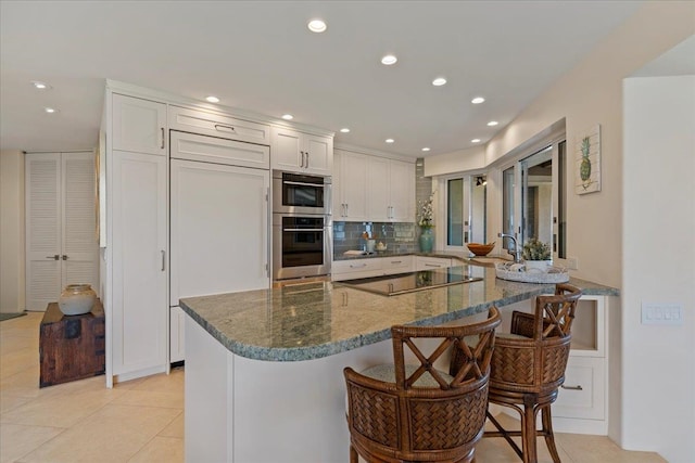 kitchen featuring black electric cooktop, light tile patterned floors, kitchen peninsula, white cabinetry, and a kitchen breakfast bar