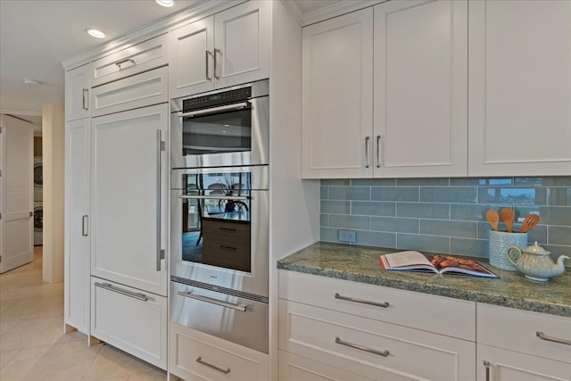 kitchen with tasteful backsplash, stainless steel double oven, dark stone countertops, light tile patterned floors, and white cabinetry