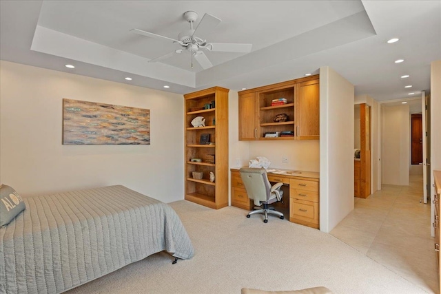 carpeted bedroom with ceiling fan, a raised ceiling, and built in desk