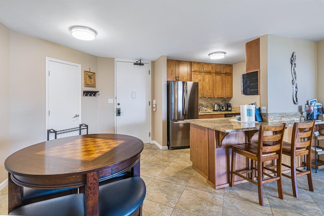 kitchen with light stone counters, backsplash, kitchen peninsula, stainless steel fridge, and light tile patterned flooring