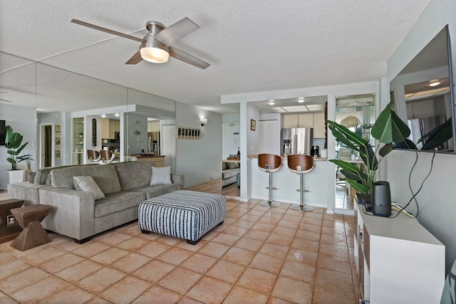 living room with ceiling fan, a textured ceiling, and light tile patterned flooring