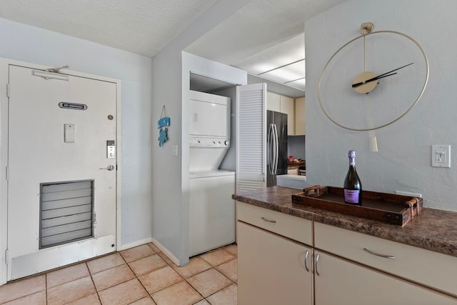 kitchen featuring stacked washer and clothes dryer, stainless steel refrigerator, a textured ceiling, and light tile patterned flooring