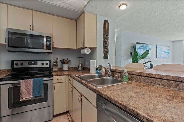 kitchen with cream cabinets, stainless steel appliances, sink, and a textured ceiling