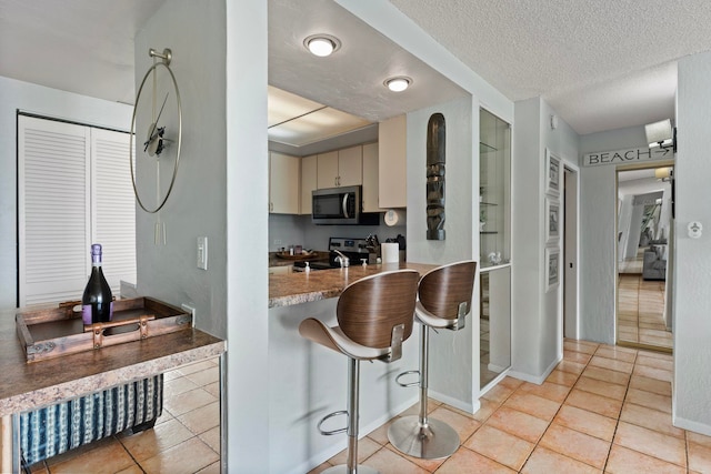 kitchen with light stone counters, light tile patterned floors, appliances with stainless steel finishes, a kitchen breakfast bar, and a textured ceiling