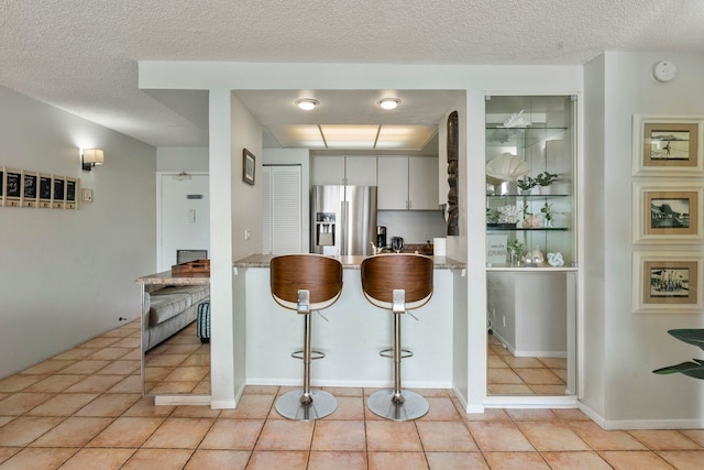 kitchen with white cabinets, stainless steel fridge with ice dispenser, light tile patterned floors, and a textured ceiling