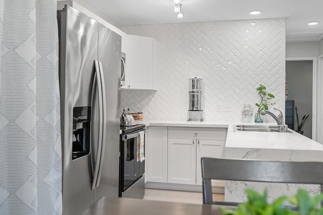 kitchen featuring backsplash, light stone countertops, stainless steel appliances, white cabinetry, and a sink