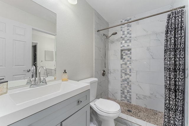 bathroom with a textured wall, toilet, vanity, and a tile shower