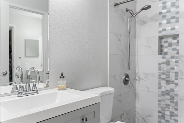 full bath featuring toilet, tiled shower, vanity, and a textured wall