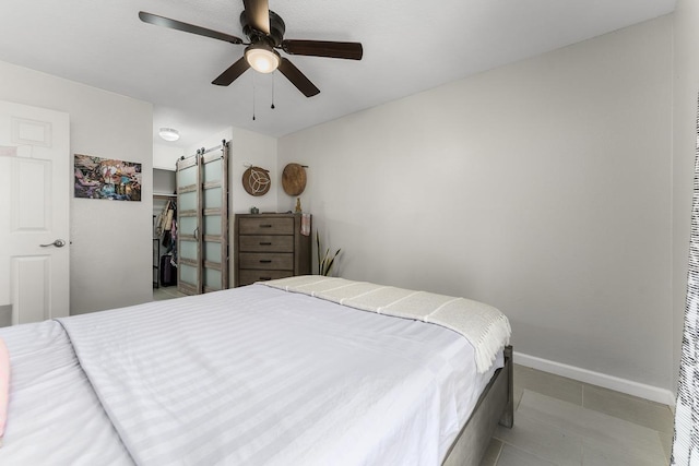 tiled bedroom featuring a barn door, baseboards, and a ceiling fan