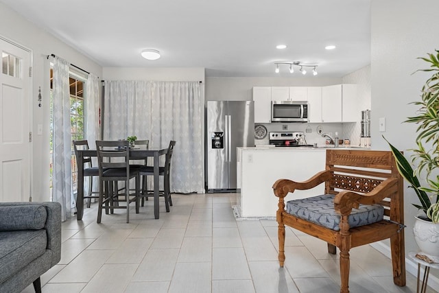 kitchen with a peninsula, light tile patterned flooring, light countertops, appliances with stainless steel finishes, and white cabinetry