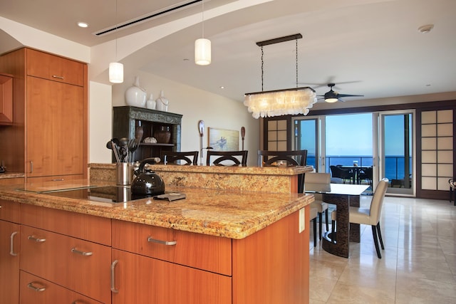 kitchen with pendant lighting, ceiling fan with notable chandelier, a water view, and light stone counters