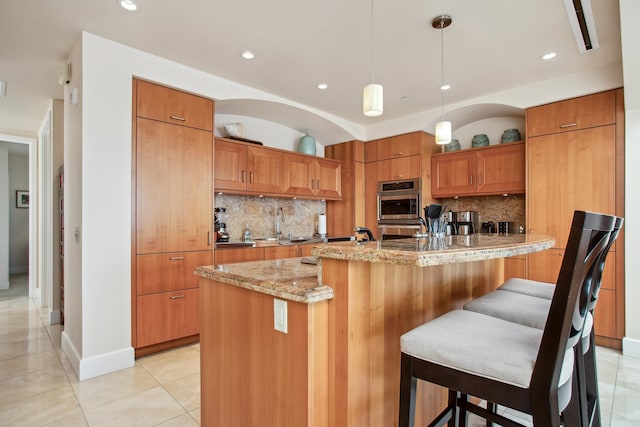 kitchen featuring a kitchen island with sink, stainless steel double oven, backsplash, and light stone countertops