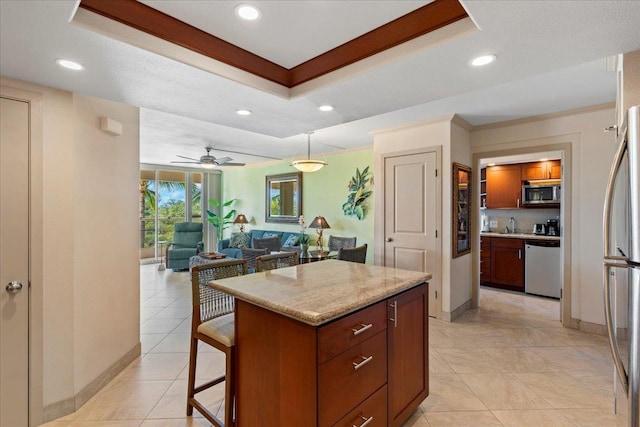 kitchen with stainless steel appliances, a tray ceiling, ceiling fan, a center island, and hanging light fixtures