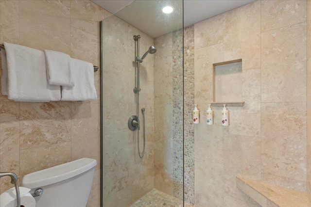 bathroom featuring toilet, tiled shower, and tile walls