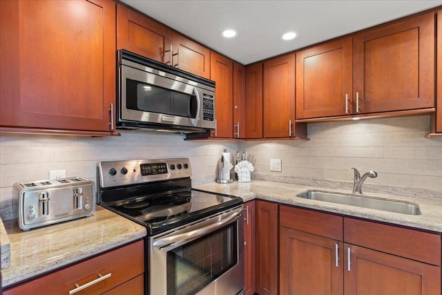 kitchen with stainless steel appliances, light stone counters, tasteful backsplash, and sink