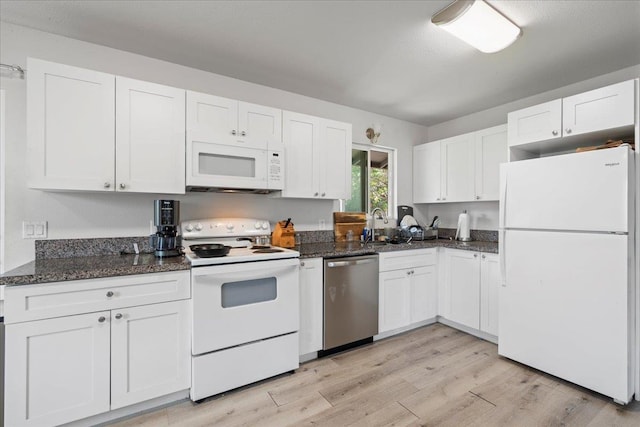 kitchen featuring dark stone counters, white cabinets, light wood finished floors, and white appliances