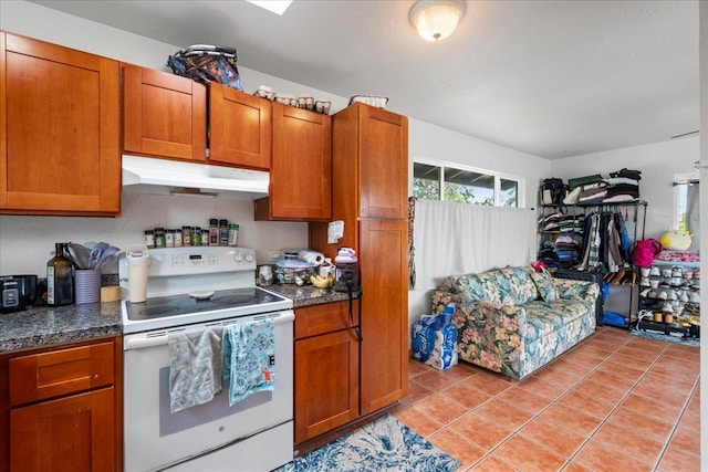 kitchen with electric range, dark countertops, brown cabinets, light tile patterned floors, and under cabinet range hood