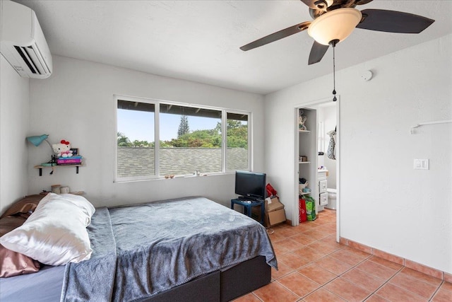 bedroom with a wall unit AC, a ceiling fan, baseboards, ensuite bathroom, and light tile patterned flooring