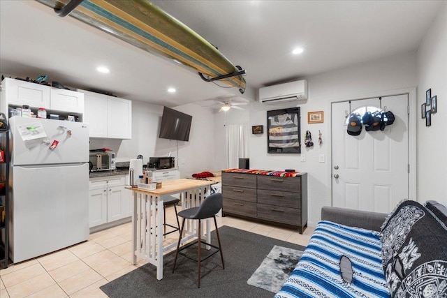 kitchen featuring freestanding refrigerator, black microwave, a wall mounted AC, white cabinets, and light tile patterned floors