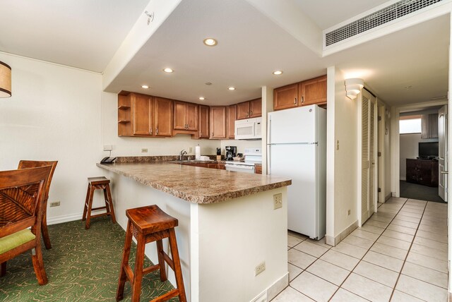 kitchen featuring a kitchen bar, light tile patterned floors, sink, kitchen peninsula, and white appliances